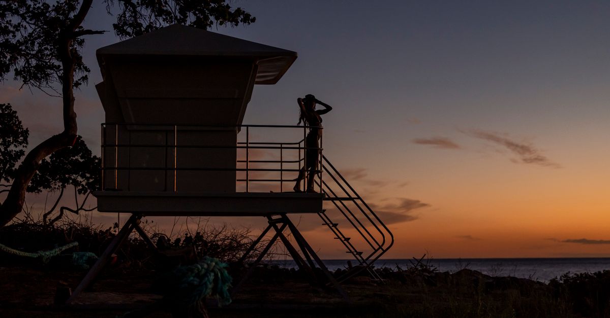 A scenic view of a lifeguard tower silhouette against a vibrant sunset sky by the ocean.