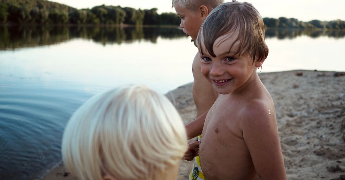 Three boys playing joyfully at a lakeside beach during summer in Ozyory, Russia.