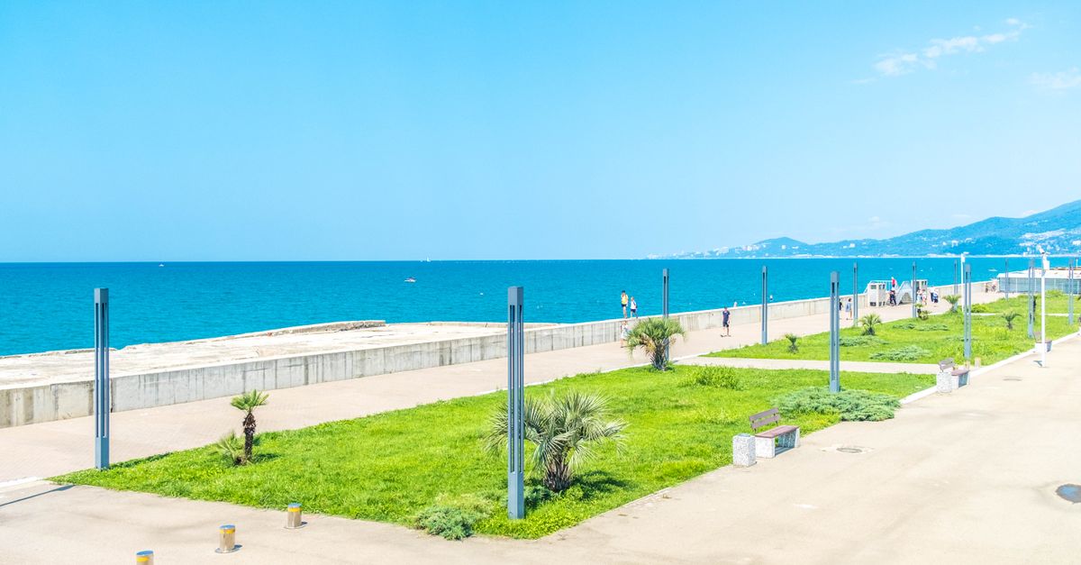 Bright, sunny view of the Sochi seafront promenade by the Black Sea with clear blue sky.