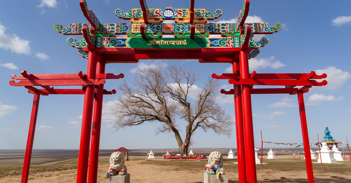 Vibrant Buddhist archway frames a tree on a vast steppe landscape under a blue sky.