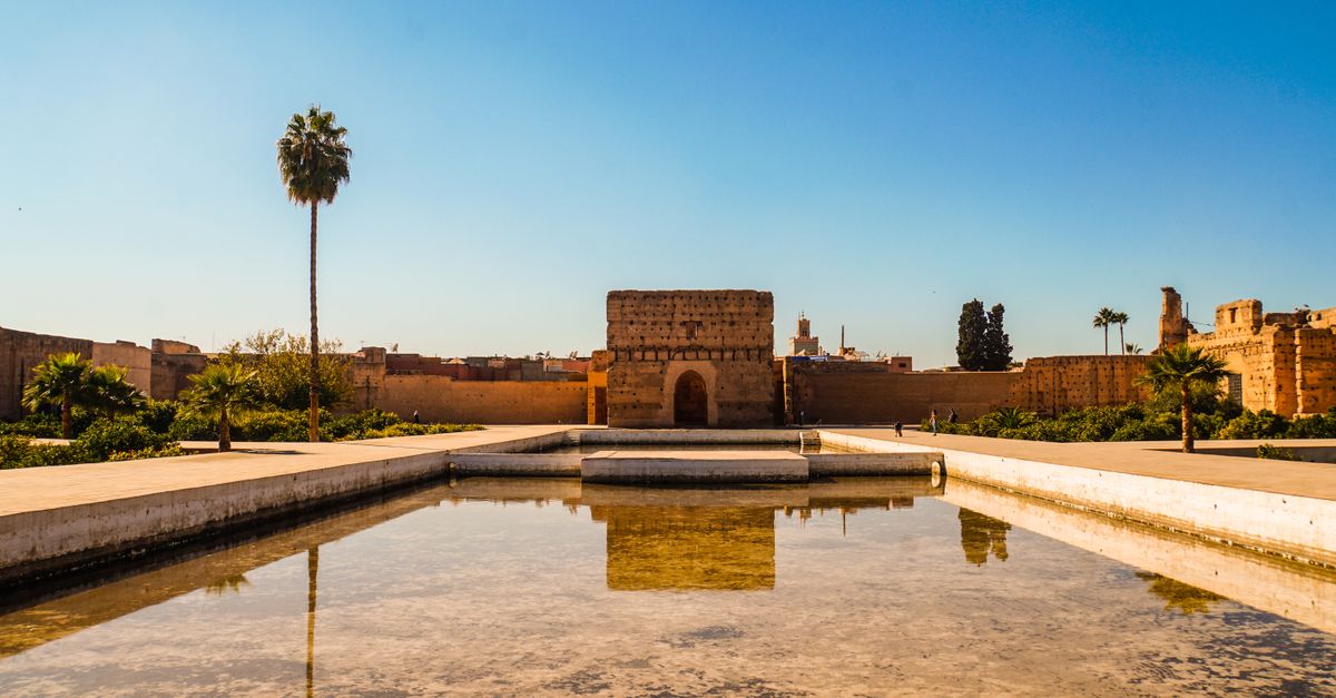 El Badi Palace in Marrakech under a clear blue sky with a reflecting pool in the foreground.
