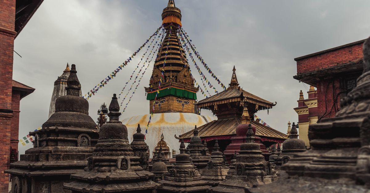 Ancient Swayambhunath Stupa in Kathmandu with vibrant prayer flags under cloudy sky.