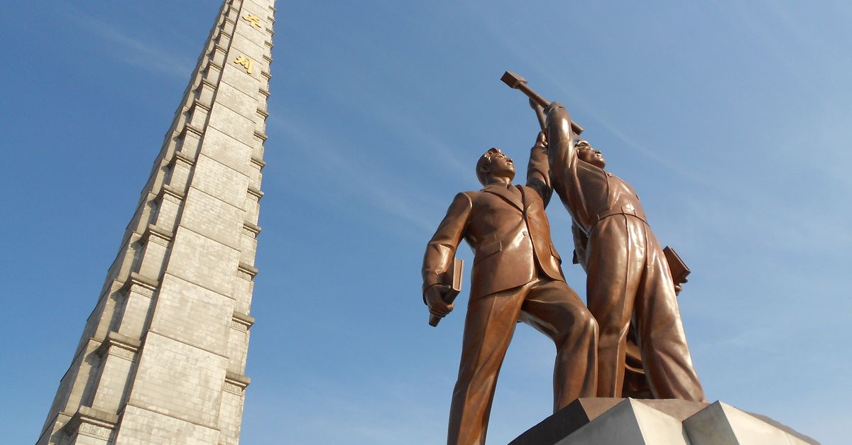 Low angle view of Juche Tower and worker statues against a clear blue sky in Pyongyang, North Korea.