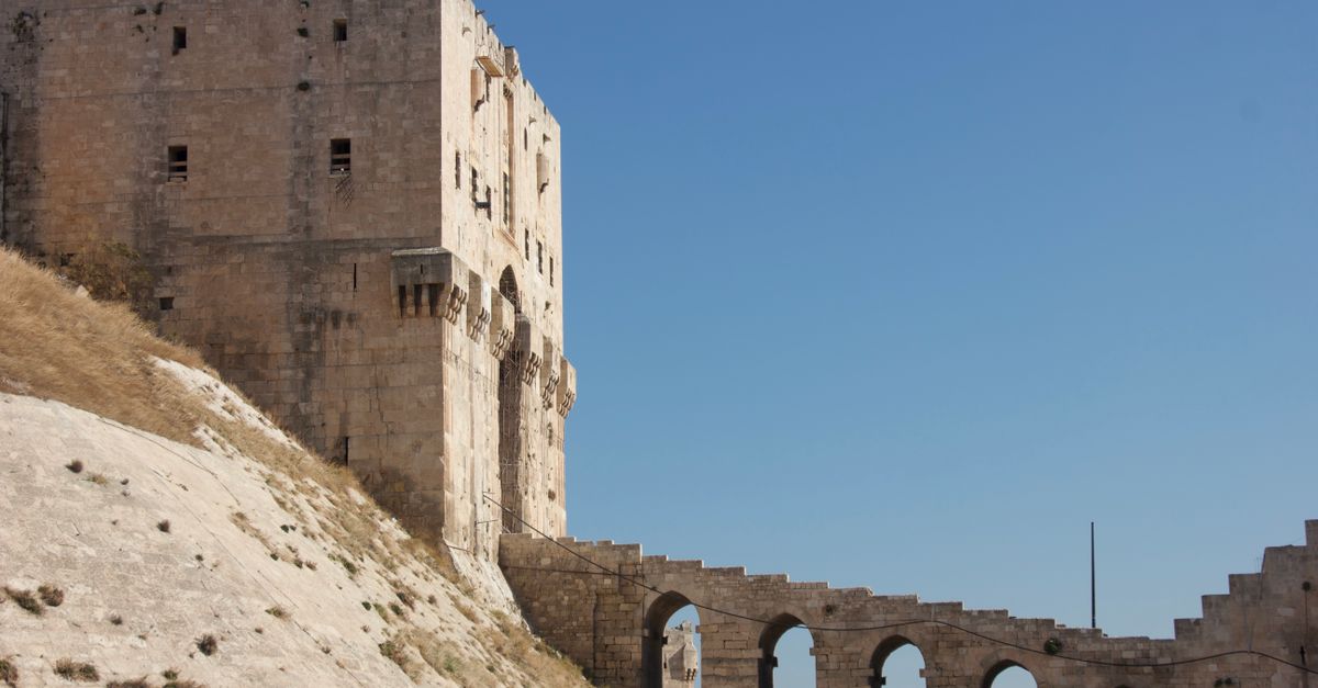 Ancient castle with arched structures under clear blue sky, featuring historical architecture.