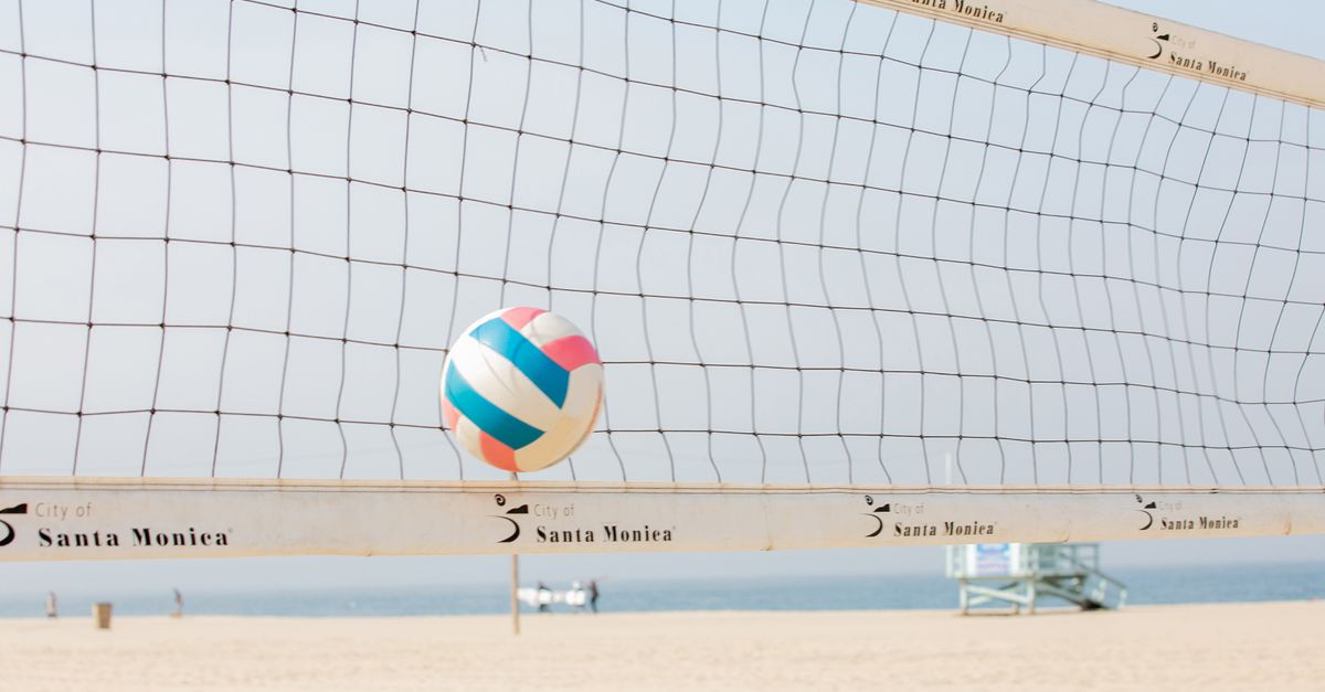 Colorful volleyball in mid-air at Santa Monica beach with net in foreground.