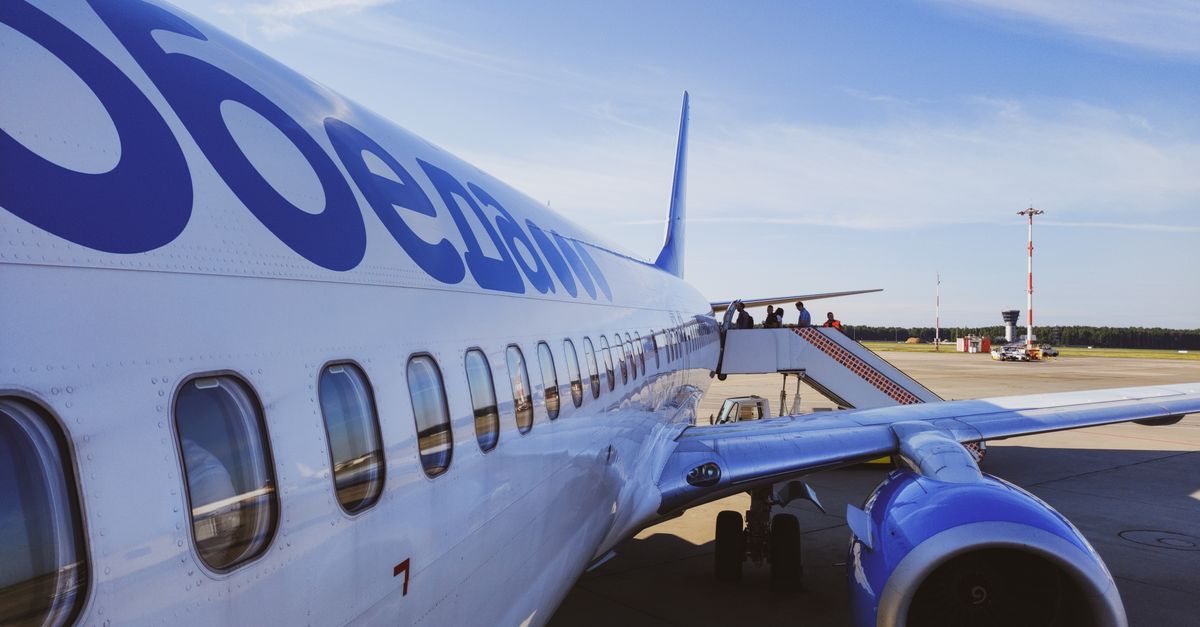 Side view of a commercial airplane with passengers boarding at a sunny airport.