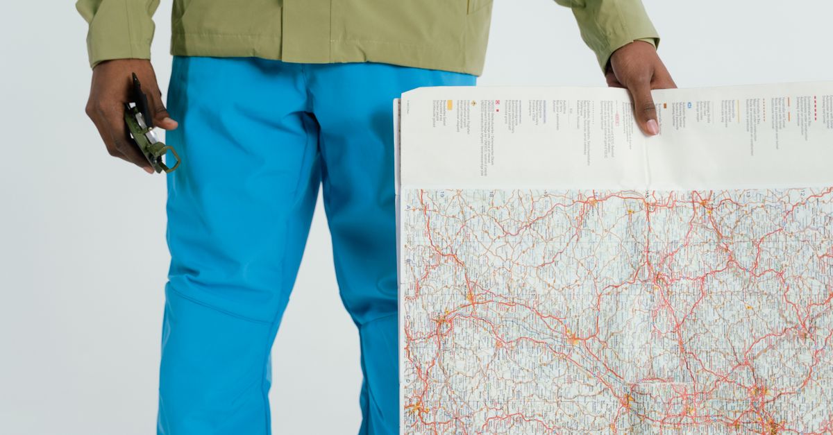 Man in outdoor attire holding a map and compass, prepared for exploration.