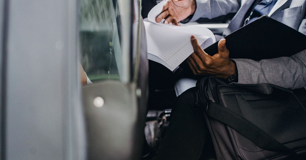 Busy crop anonymous African American male preparing important papers in folder while sitting in automobile