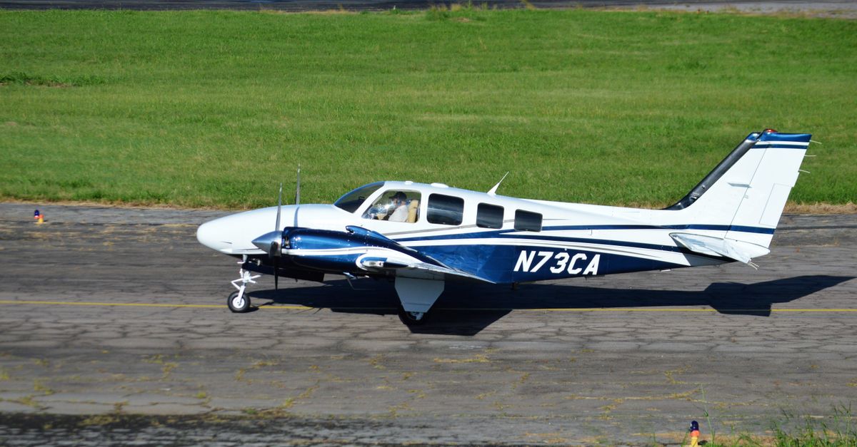 A small aircraft with registration N73CA taxiing on a sunny runway with green grass.