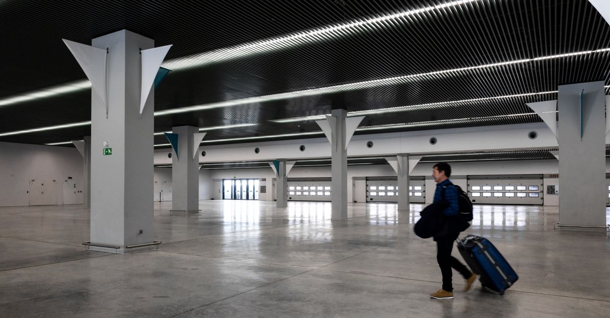 A man with luggage walking through a spacious, modern, empty airport hall.