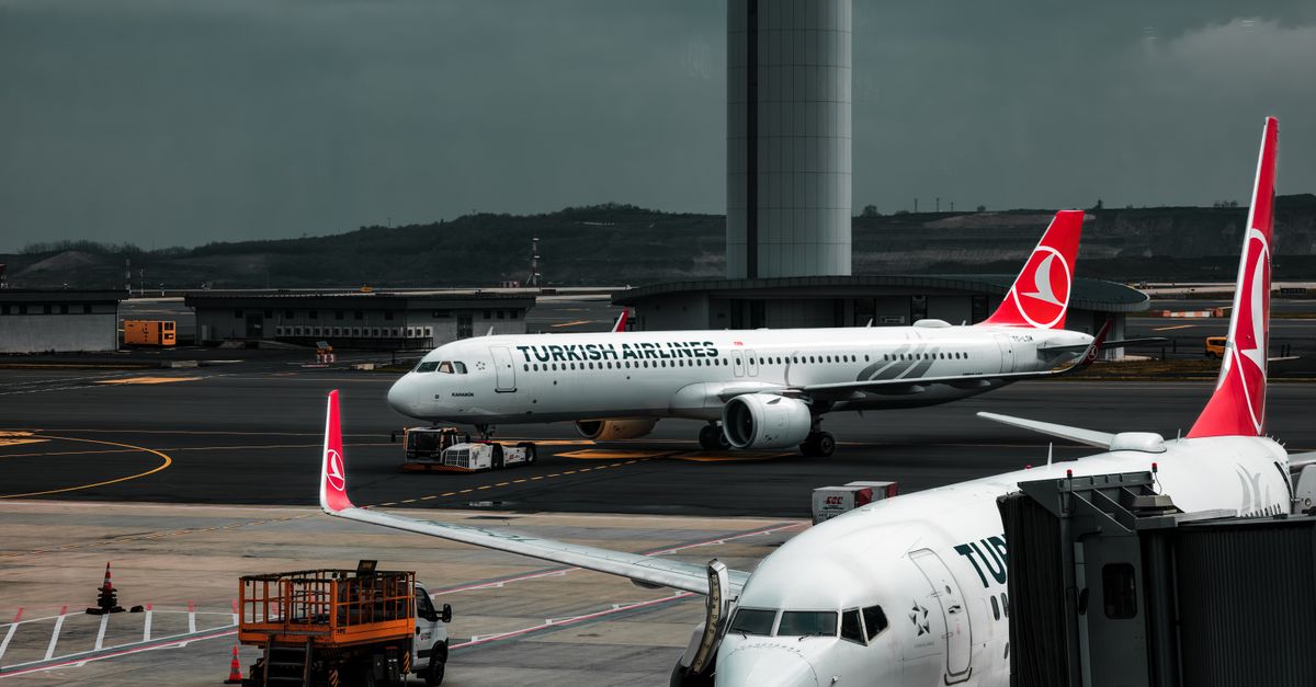 Turkish Airlines planes parked at an airport with a control tower in the background.