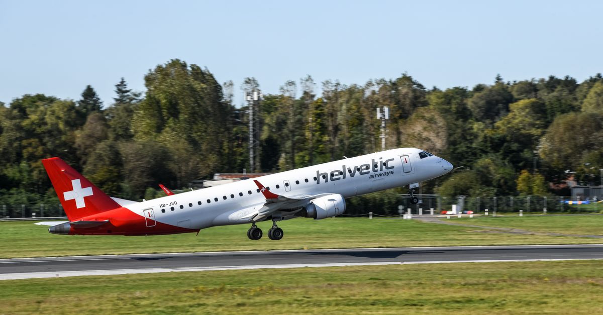 Helvetic Airways plane taking off from a runway surrounded by greenery.
