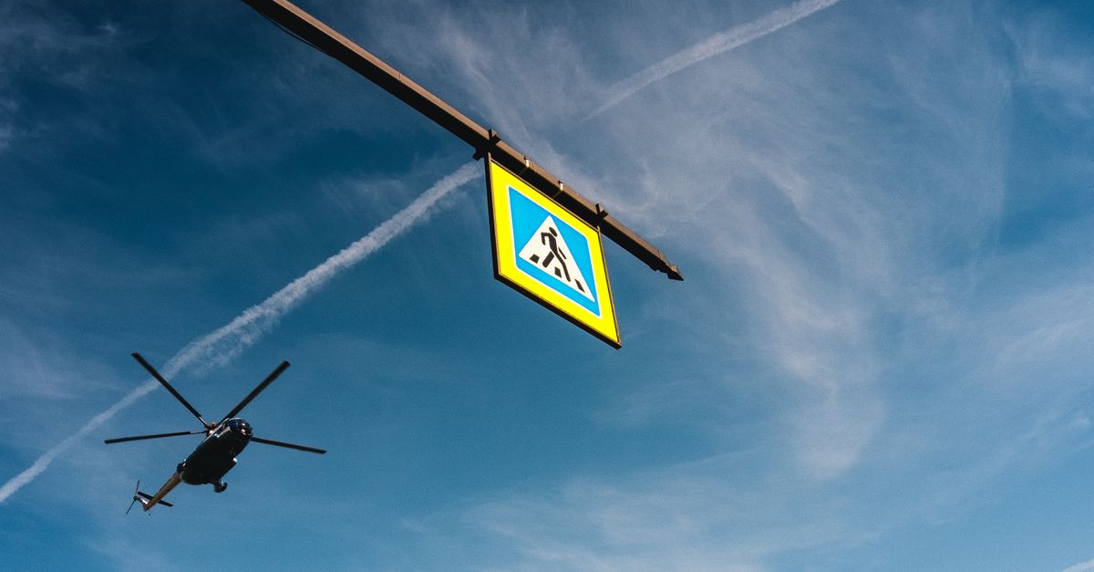 A helicopter flies beside a pedestrian crossing sign against a clear blue sky in Saint Petersburg, Russia.