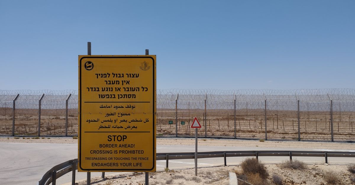 A warning sign prohibiting crossing near a desert border area with clear blue sky.