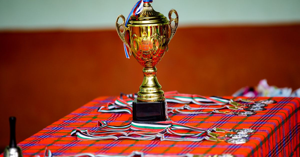 Golden trophy with ribbons and medals on a checkered table, symbolizing victory and achievement.