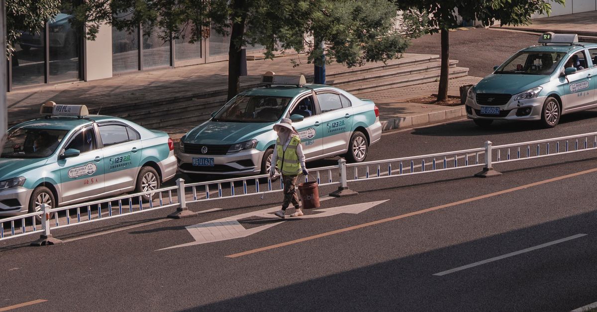 A city street with parked taxis and a pedestrian crossing the road in daylight.