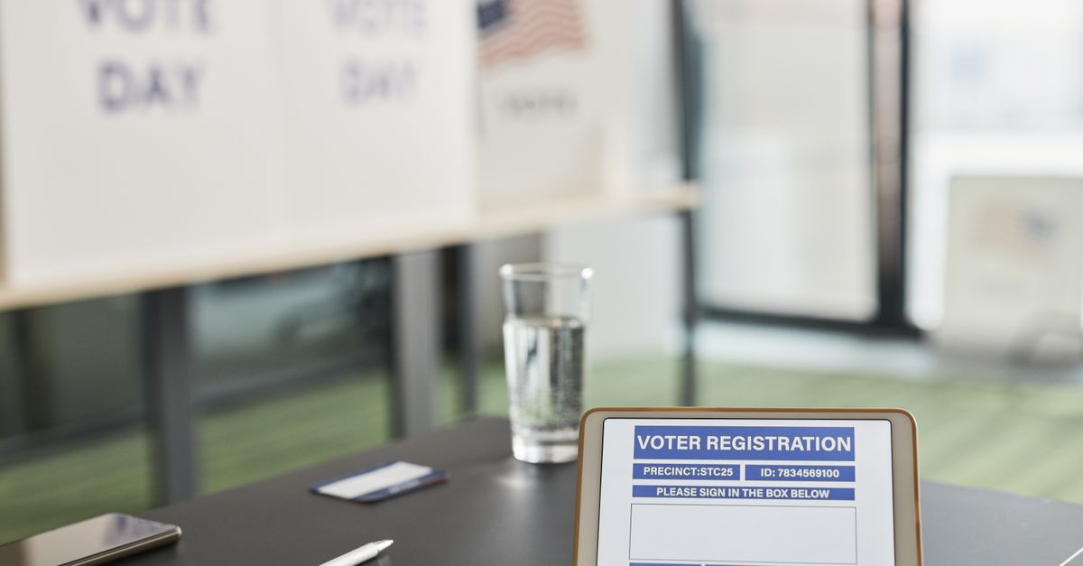 Tablet displaying digital voter registration at indoor voting station with vote day signs.