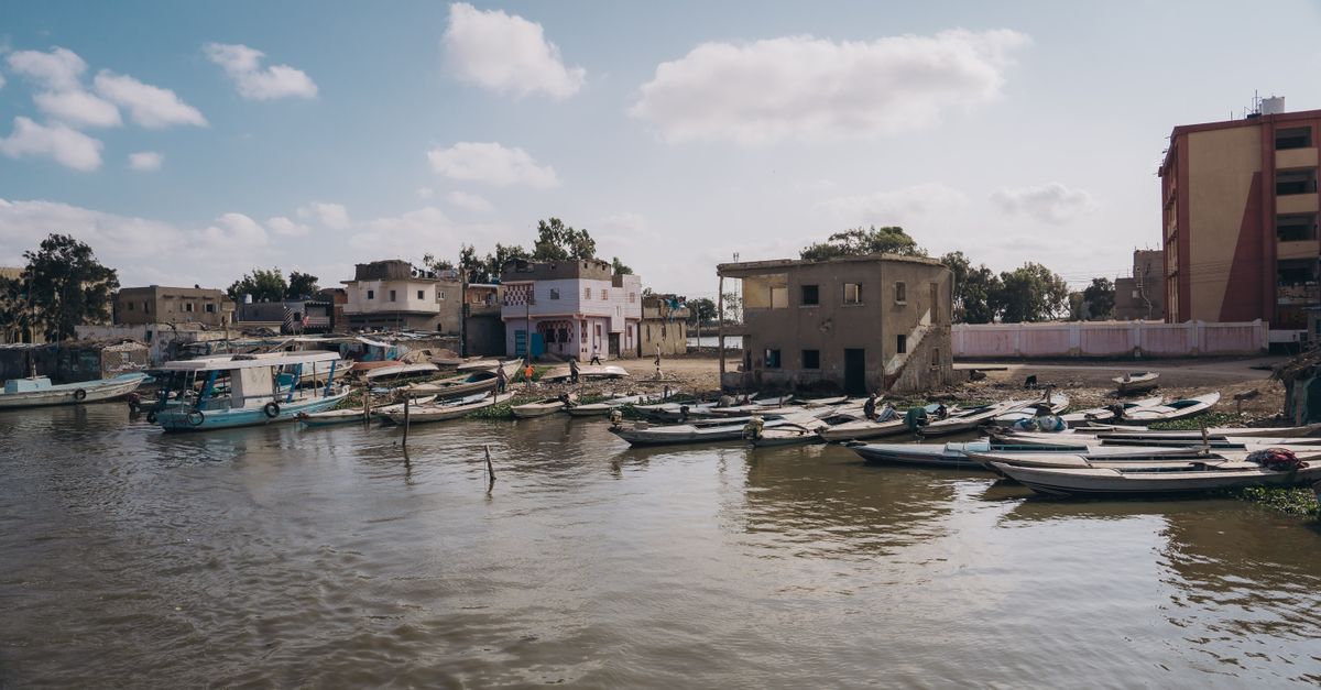 Tranquil waterfront scene in Kafr El-Shaikh, Egypt with boats and historic buildings.