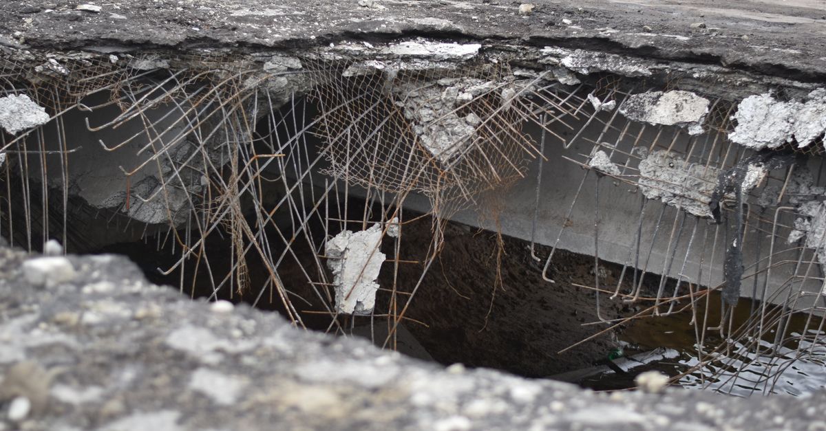 A close-up of a damaged concrete structure with exposed rebar, depicting urban decay.