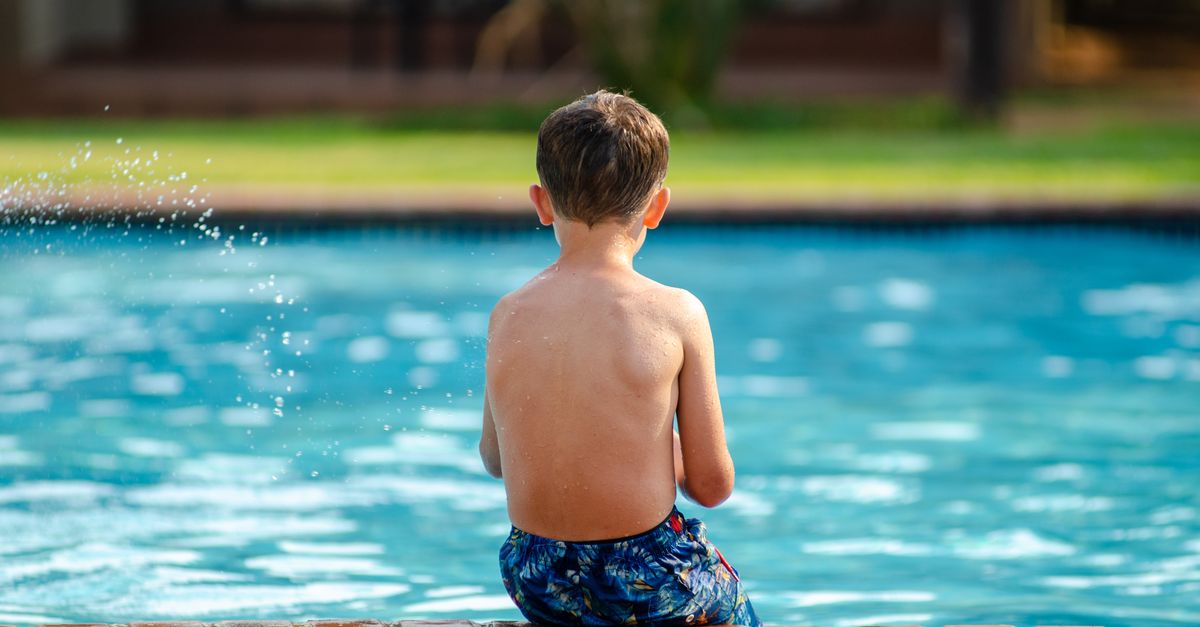 A child sits on the poolside, enjoying a sunny day outdoors.
