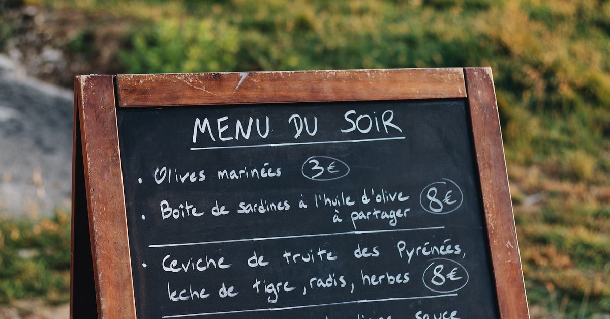 Chalkboard menu stand listing French dishes and prices in an outdoor setting.