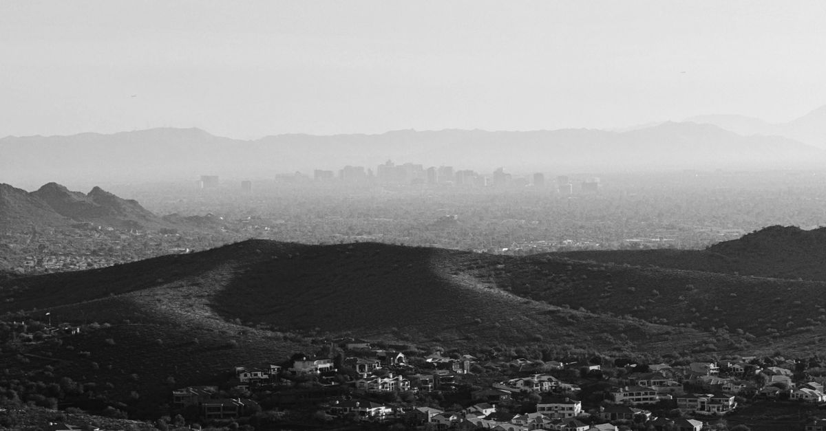 A grayscale cityscape view from the mountains with urban skyline in the distance.