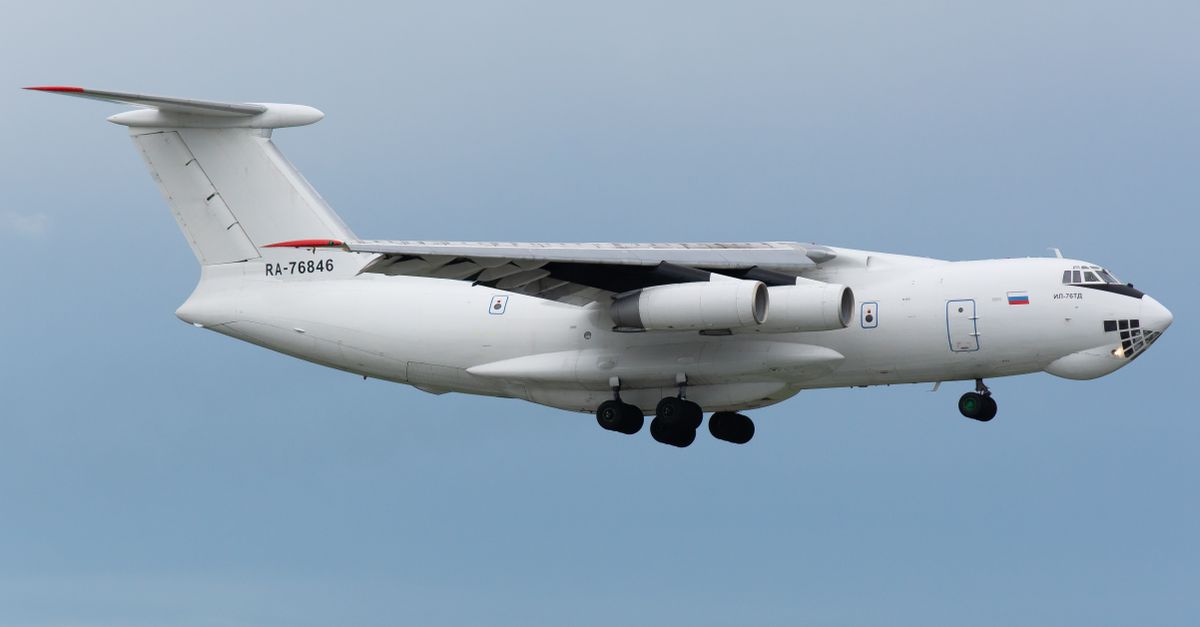 White IL-76 cargo aircraft with visible markings flying against a clear sky.