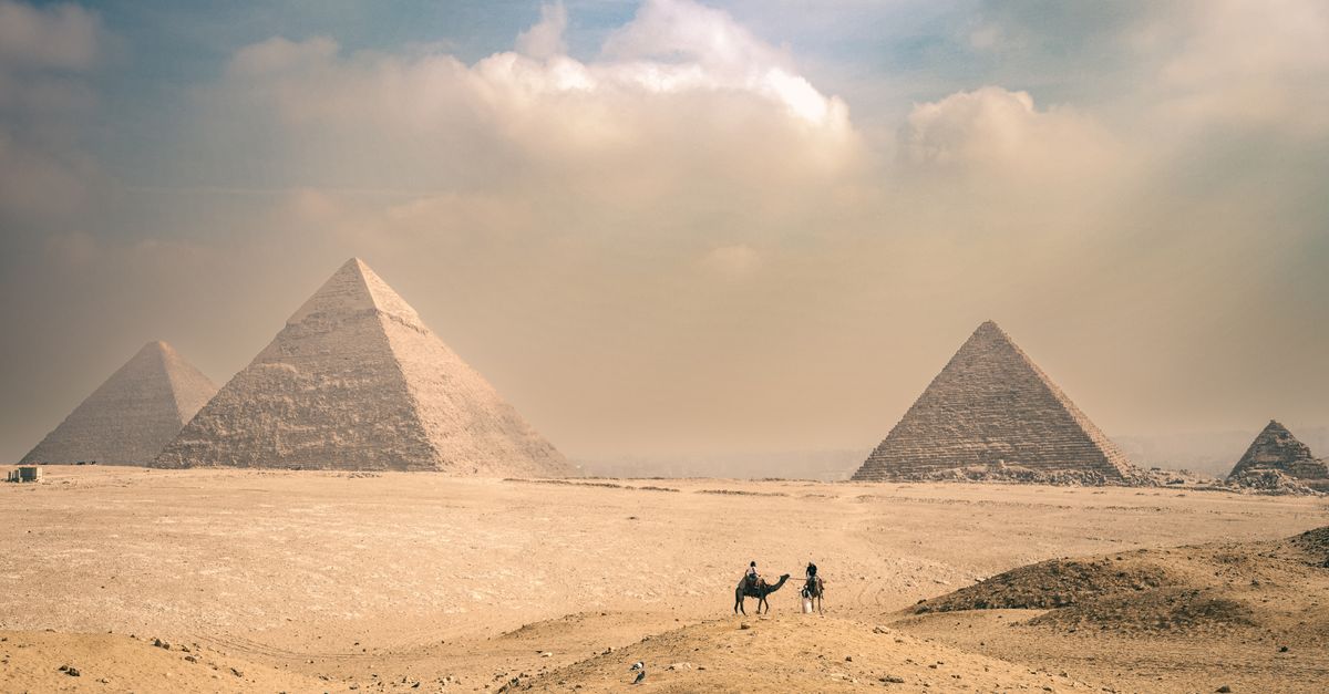 Explore the majestic Pyramids of Giza under a sunny sky with distant travelers on camels.