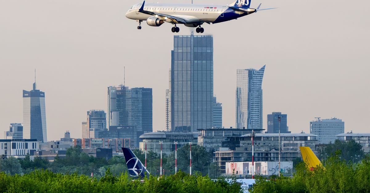 Airplane approaching landing over Warsaw's cityscape with modern skyscrapers in view.