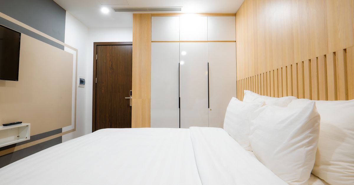 A modern hotel room with minimalist and cozy decor featuring a comfortable bed and wooden panels.