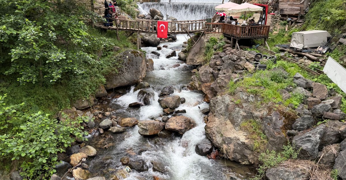 Beautiful waterfall and river scenery with a wooden bridge showcasing a Turkish flag, captured in nature.