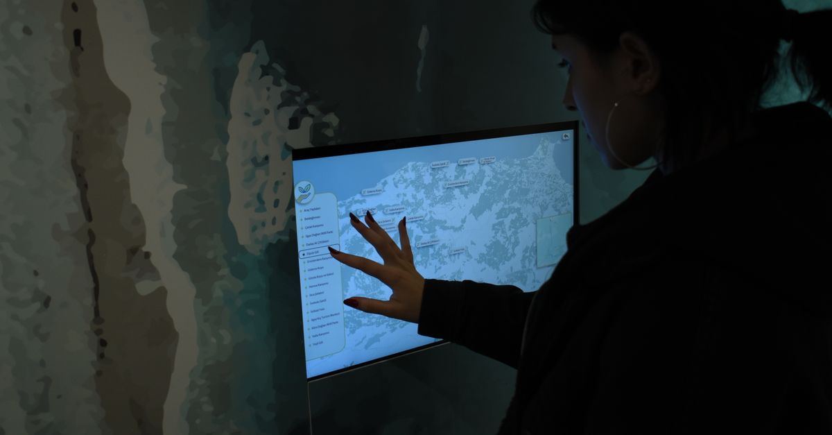 Silhouette of person interacting with a touchscreen map in a dark room.