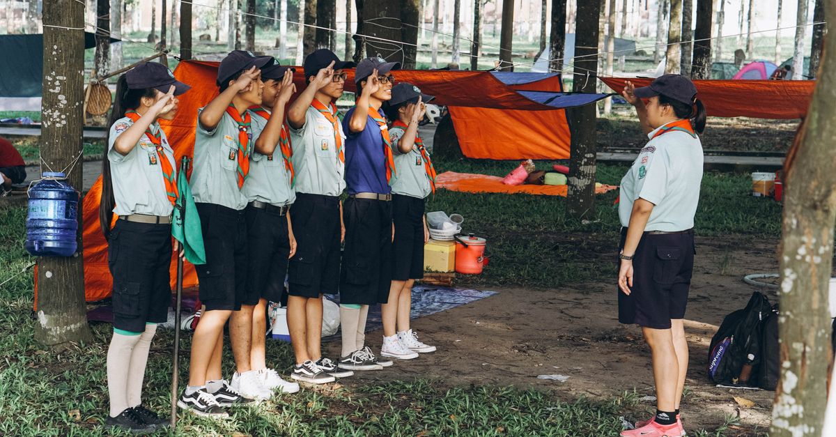 A group of young scouts practicing salute during a camping trip in a forest.