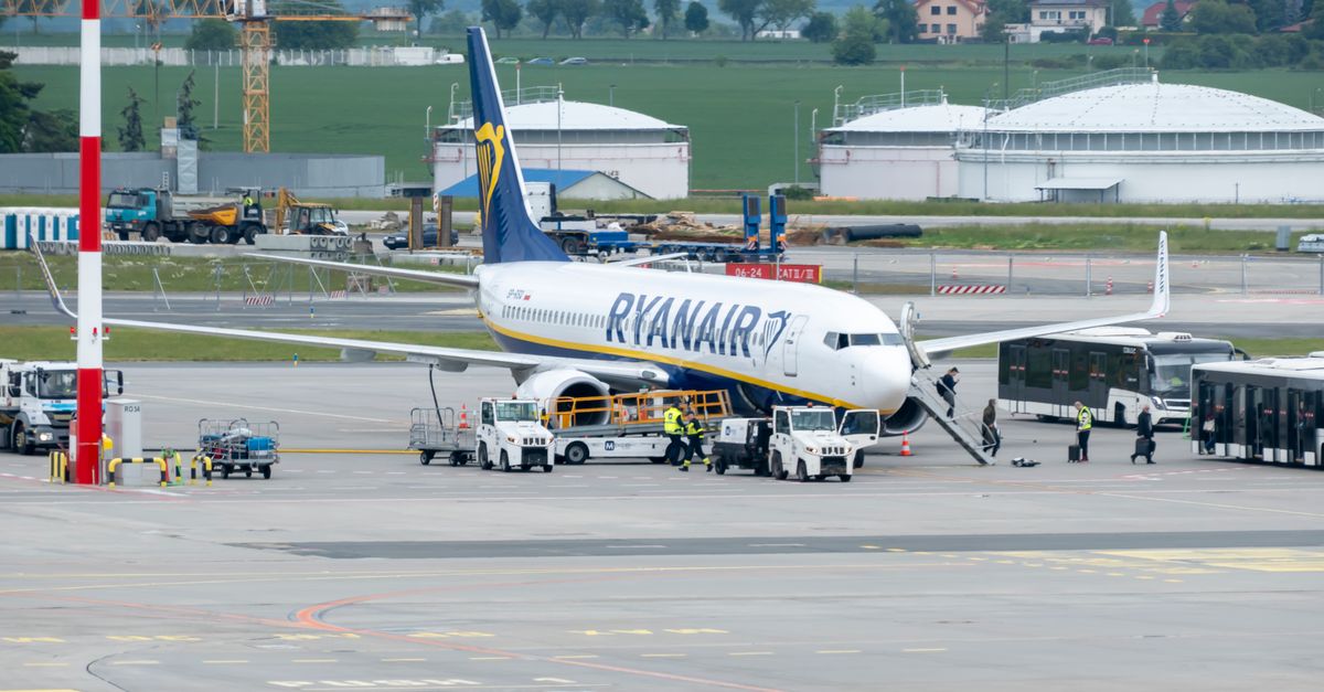 Passengers and crew prepare a Ryanair plane for departure at a bustling airport terminal.