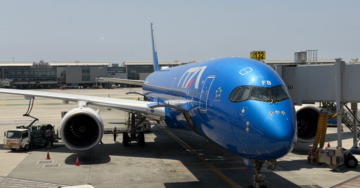 A sleek blue commercial jet parked at a boarding gate in Los Angeles International Airport.