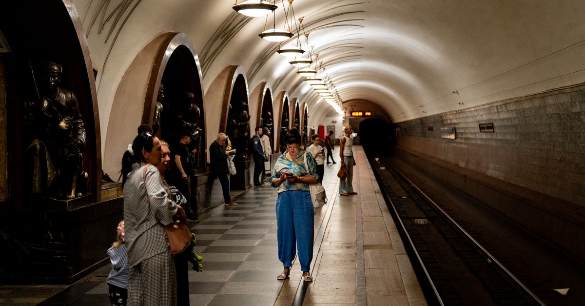 Travelers wait on a Moscow Metro station platform, showcasing its architectural beauty.