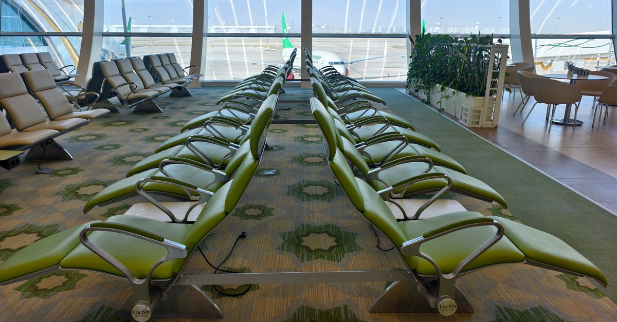 Modern airport seating area with green chairs and expansive windows offering a runway view.