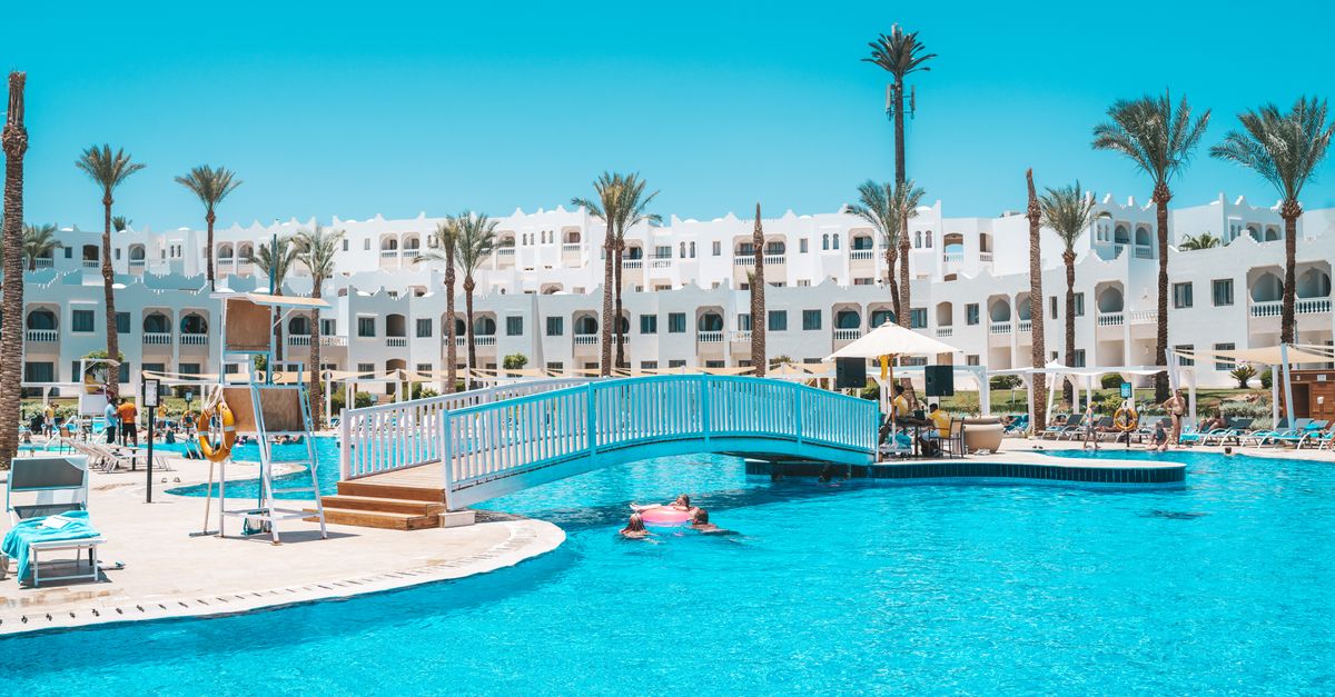 Scenic view of a resort pool with a footbridge and palm trees under a clear sky.