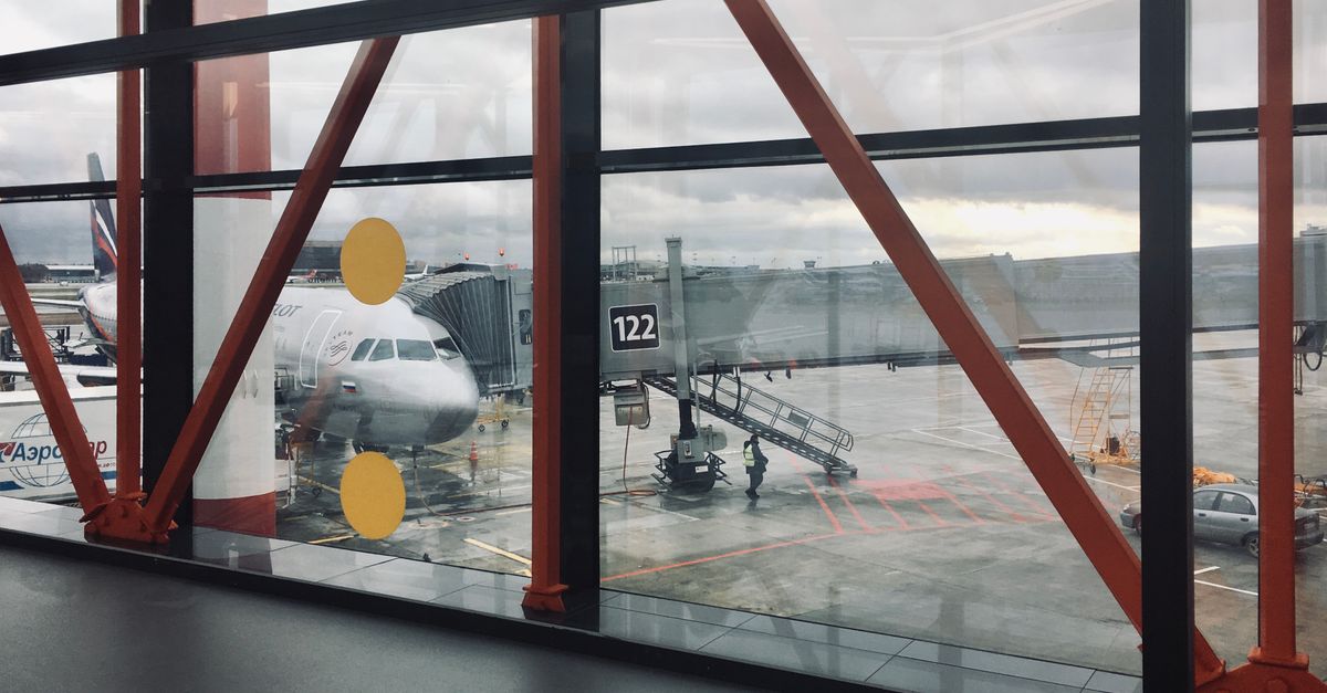 View of a commercial airplane parked at an airport terminal through large glass windows, showcasing airport activity.