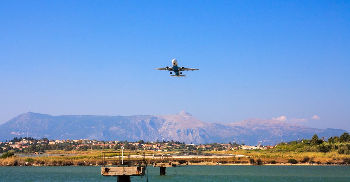 A plane flying over Corfu, Greece with mountains and water below, capturing a vibrant day scene.