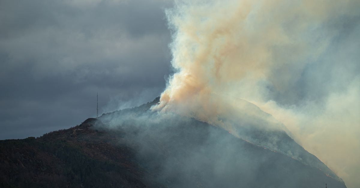 Thick smoke rises from a mountainside in Norway, creating a dramatic sky scene.