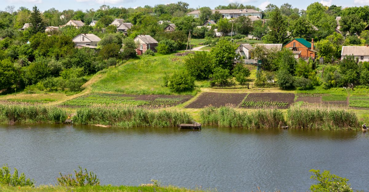 Beautiful rural landscape featuring village homes and green fields by a river under a bright sky.
