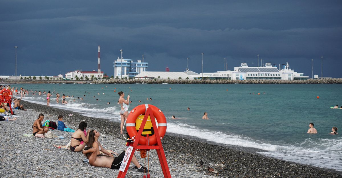 A lively summer day at Sochi beach with people enjoying the sea under a stormy sky.