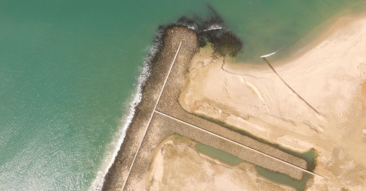 Drone aerial view of a sandy coastline and jetty in Mauritania during the day.