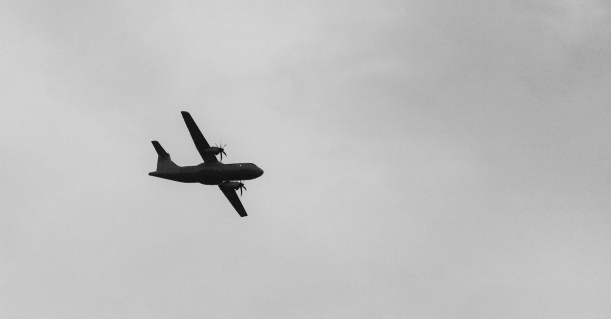 Black and white silhouette of an airplane flying against a cloudy sky.