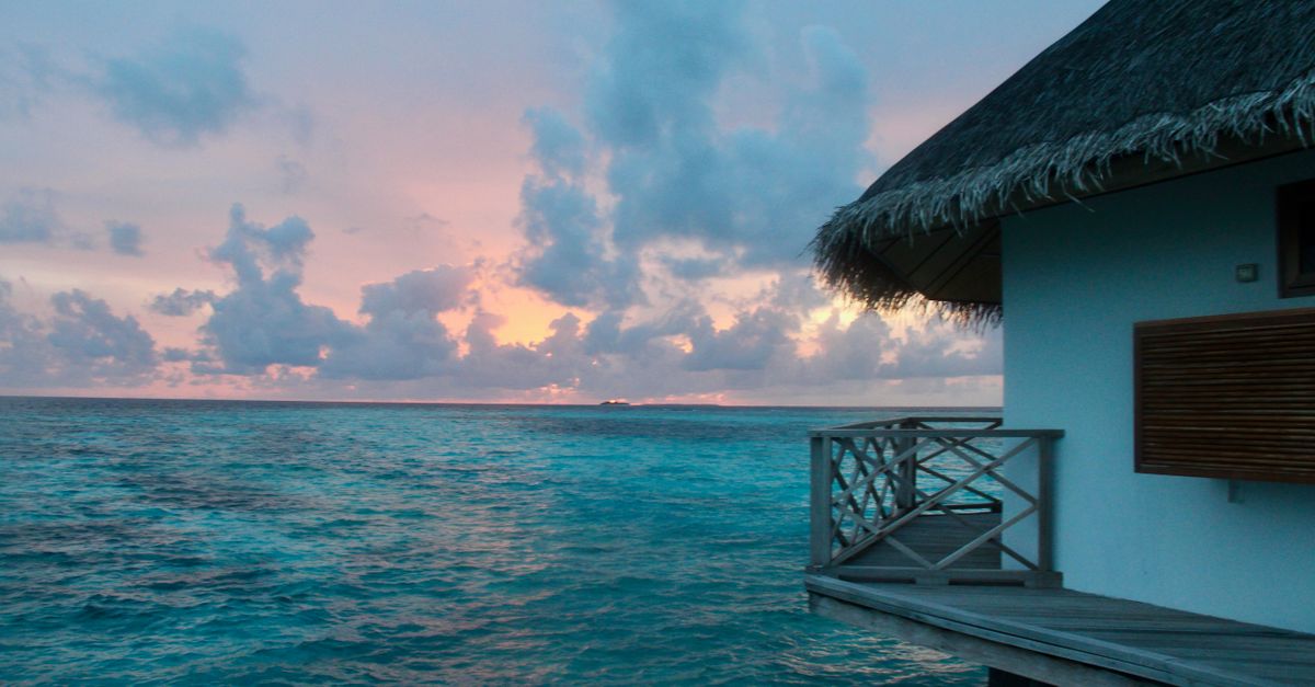 A beautiful overwater bungalow at sunset with vibrant colors in the sky and ocean.