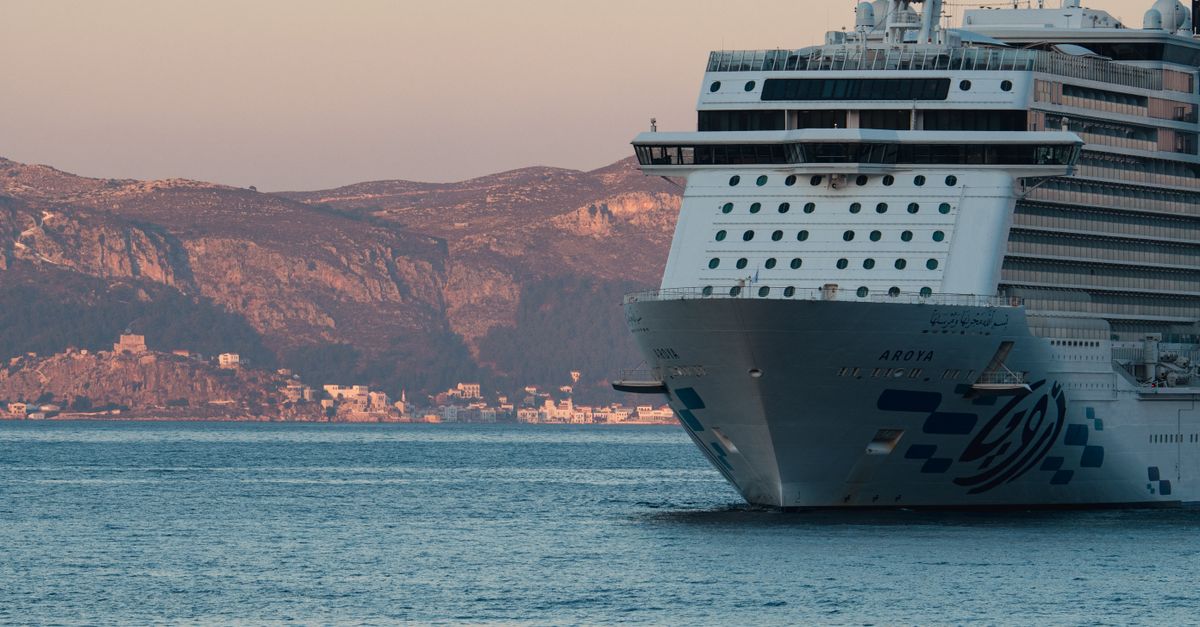 A cruise ship sails near Antalya, Türkiye, against a stunning mountain backdrop at sunset.