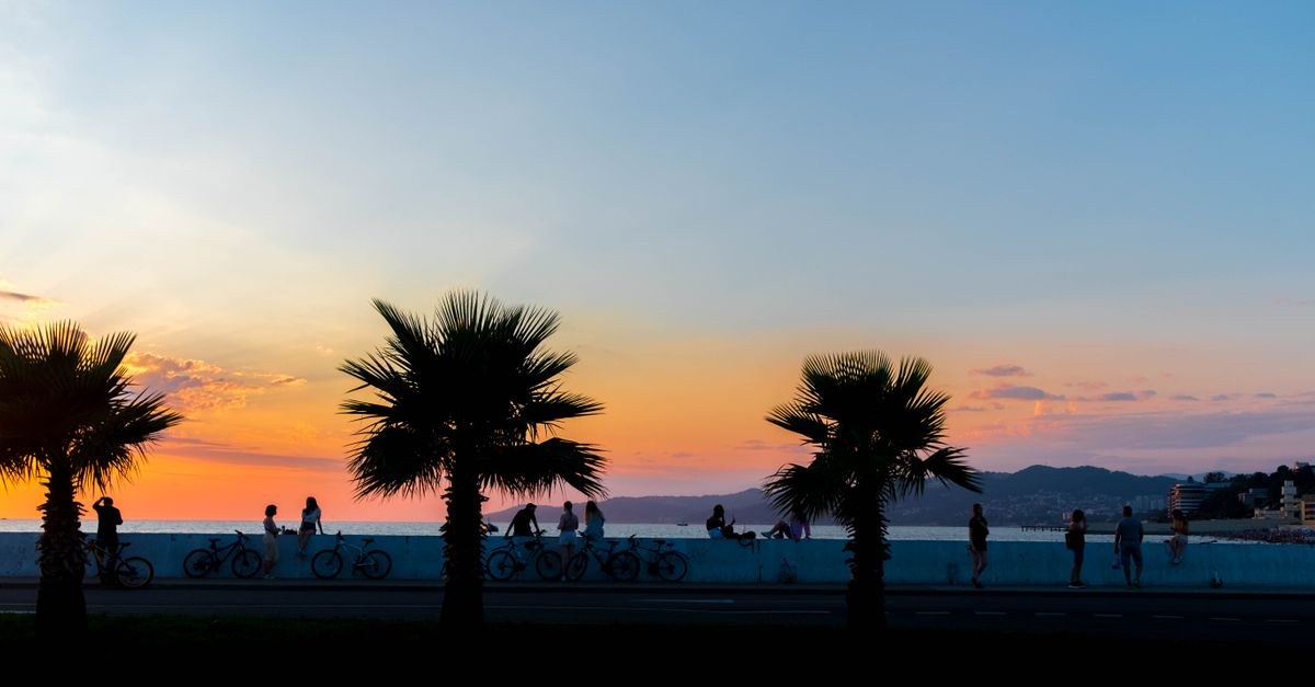 Serene sunset over Sochi with people walking along the beachfront promenade.