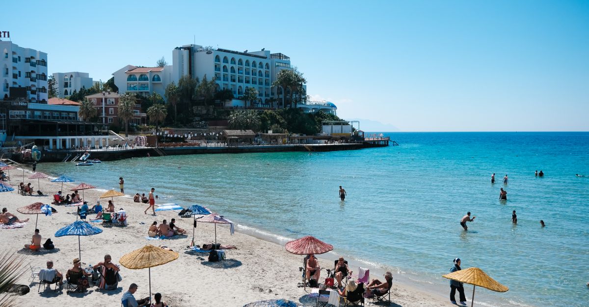 People enjoying a sunny day at a Mediterranean beach with clear blue waters and beachfront hotels.