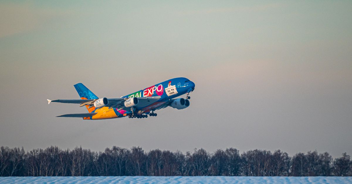 A vibrant Airbus A380 aircraft taking off over a snowy runway during the day.